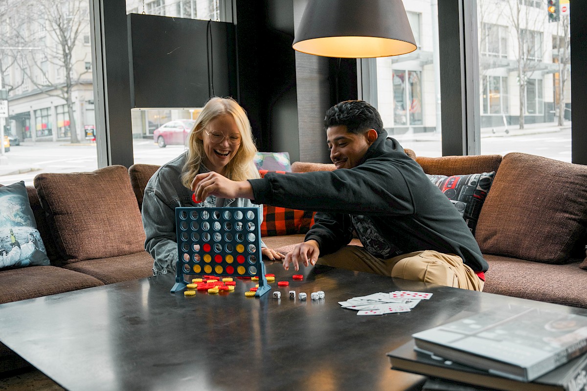 Two people are sitting on a couch in a cozy, modern living room, playing a board game together. There is a large coffee table in front of them.