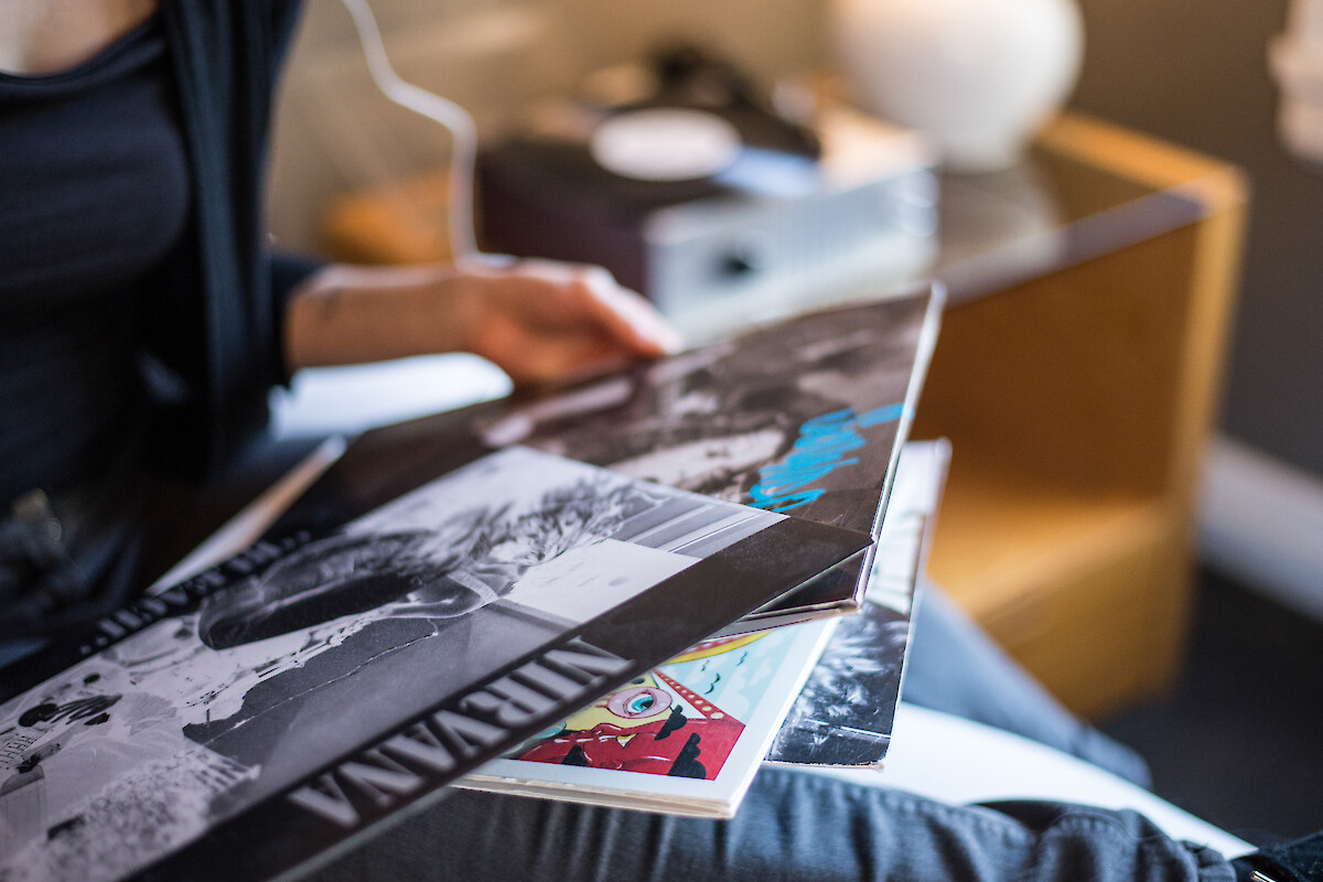 A person is holding vinyl records, with a turntable in the background.
