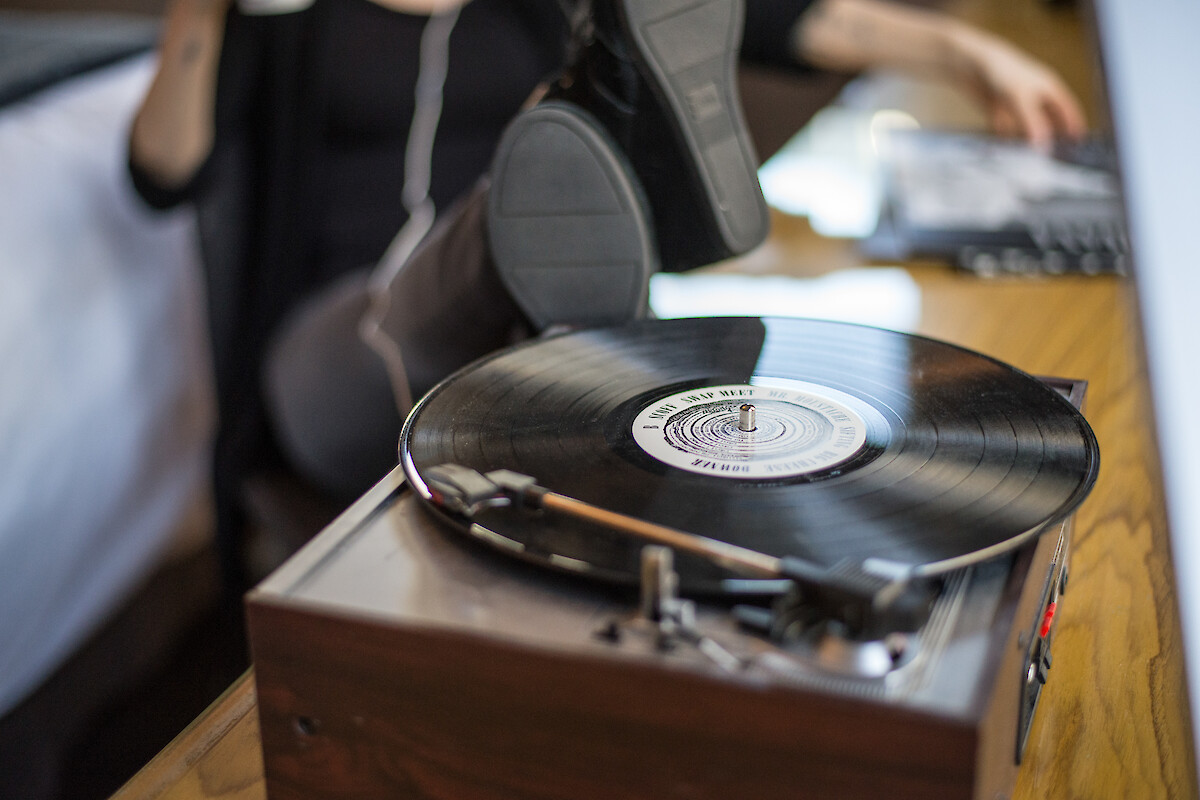 A person relaxes with feet up, listening to a vinyl record playing on a turntable, with another hand flipping through records.