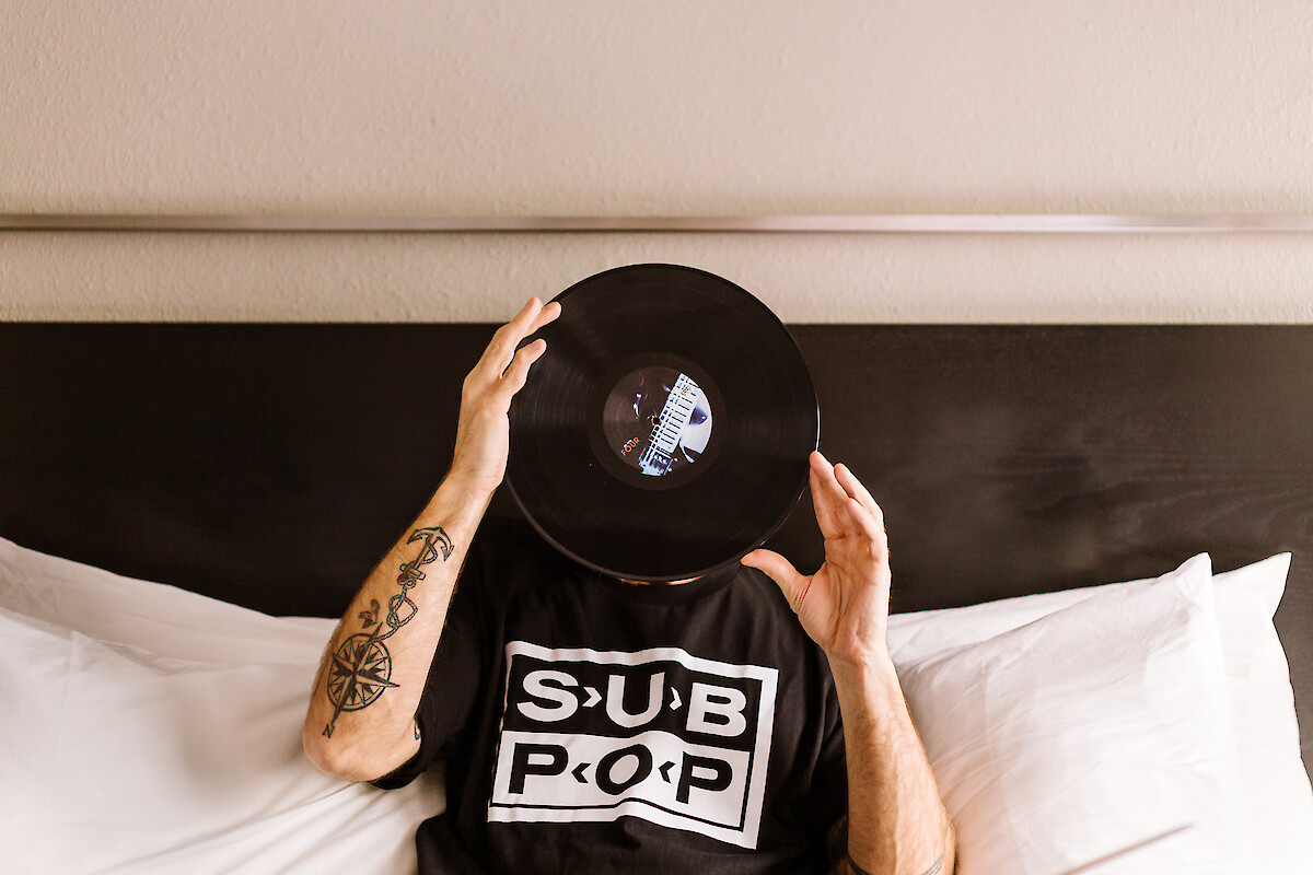 A person holds a vinyl record in front of their face, wearing a