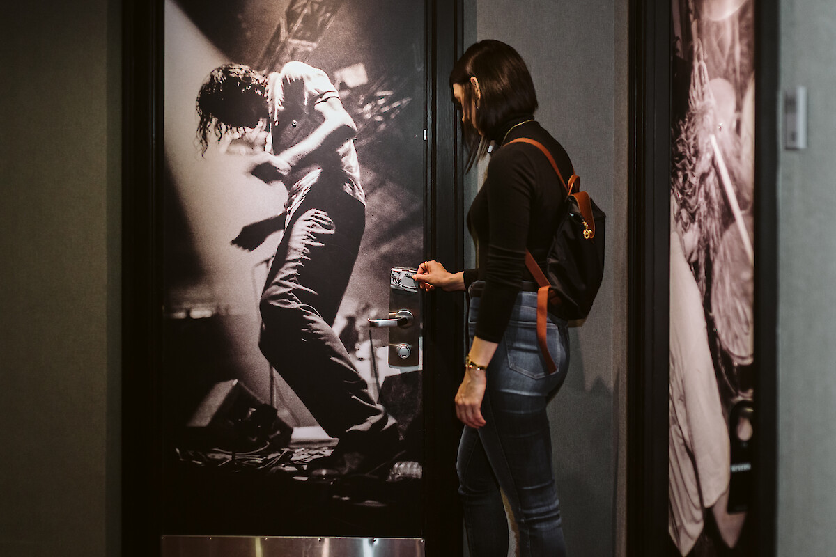 A woman is using a key card to open a door with a large black-and-white image of a rock concert on it.