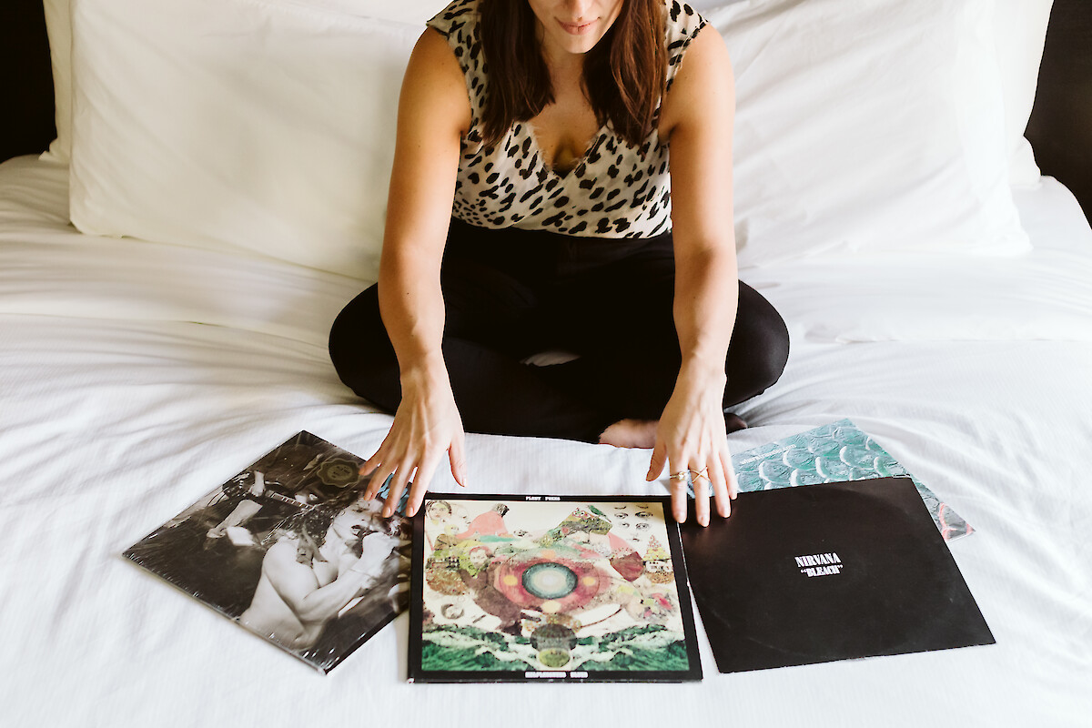 A person sits on a bed with several vinyl records, including Nirvana's