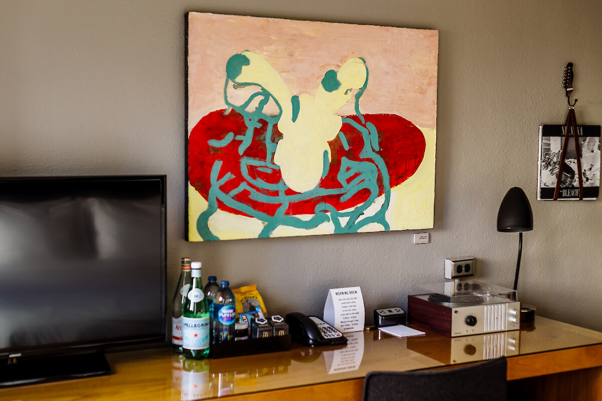 A room corner with abstract art, TV, drinks, phone, and record player. A black lamp and wall art enhance the decor.