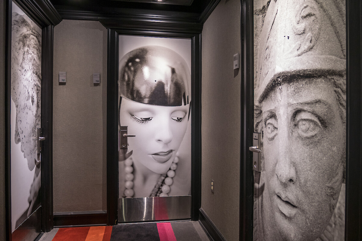 A hallway with artistic black-and-white door murals depicting faces and sculptures, alongside room numbers 721, 720, and 719.