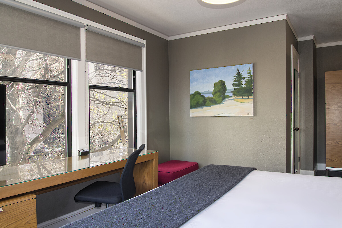 A cozy room with a bed, desk, window view, and artwork on the wall, creating a peaceful atmosphere.