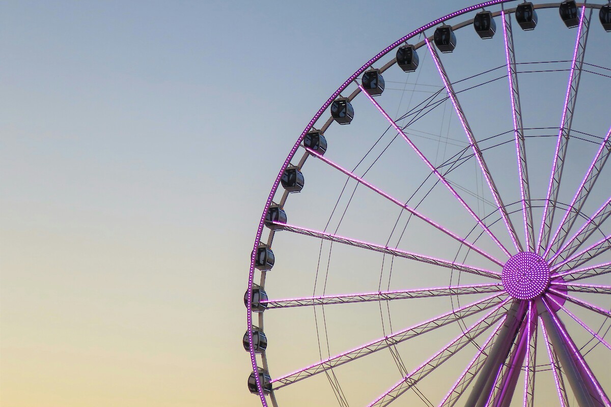 A large Ferris wheel with purple lights against a clear sky during sunset.
