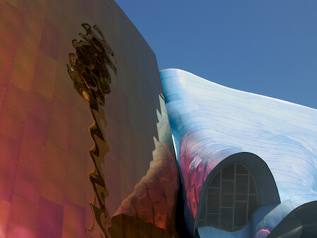 The image shows a reflective, colorful building with an undulating design against a clear blue sky, creating a modern and artistic appearance.