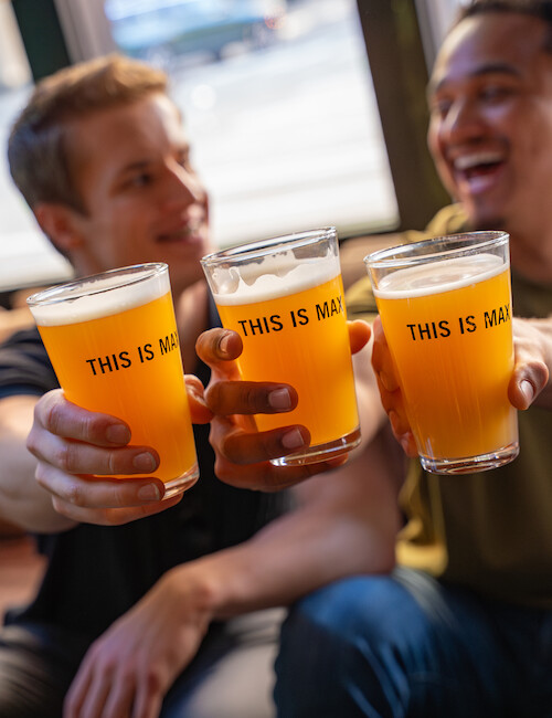 Two people are raising glasses of beer, smiling joyfully. The glasses have the words