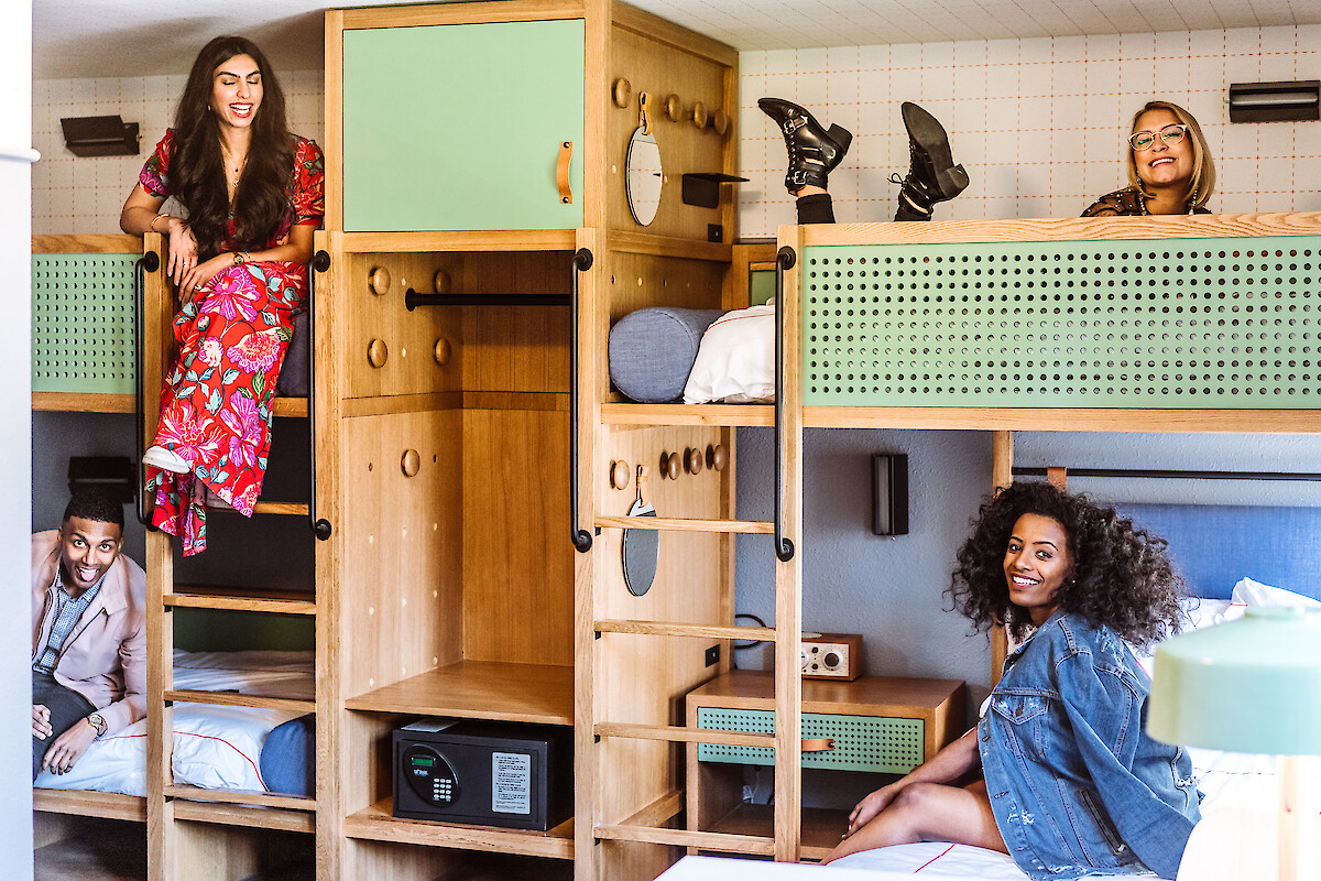 A shared dorm vibe with bunk beds, wooden shelves, and four people relaxing or peeking out, colorful outfits, cozy storage, bright vibe.