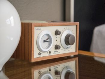 A vintage-style radio sits on a reflective surface next to a white spherical object. The radio has knobs and a dial display.