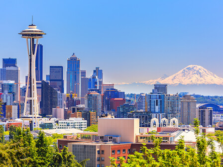 A vibrant city skyline with the Space Needle and Mount Rainier in the background on a bright, clear day.