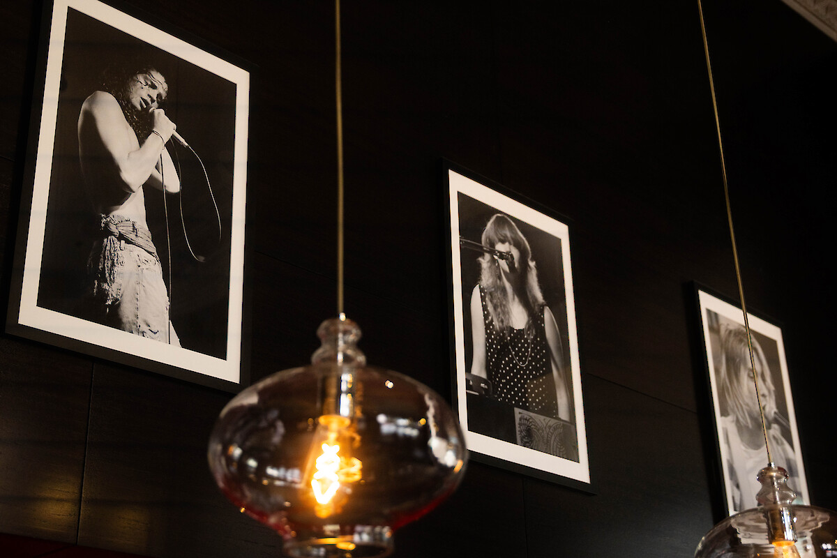 The image shows three black and white photos of singers on a dark wall with pendant lights hanging in front of them.