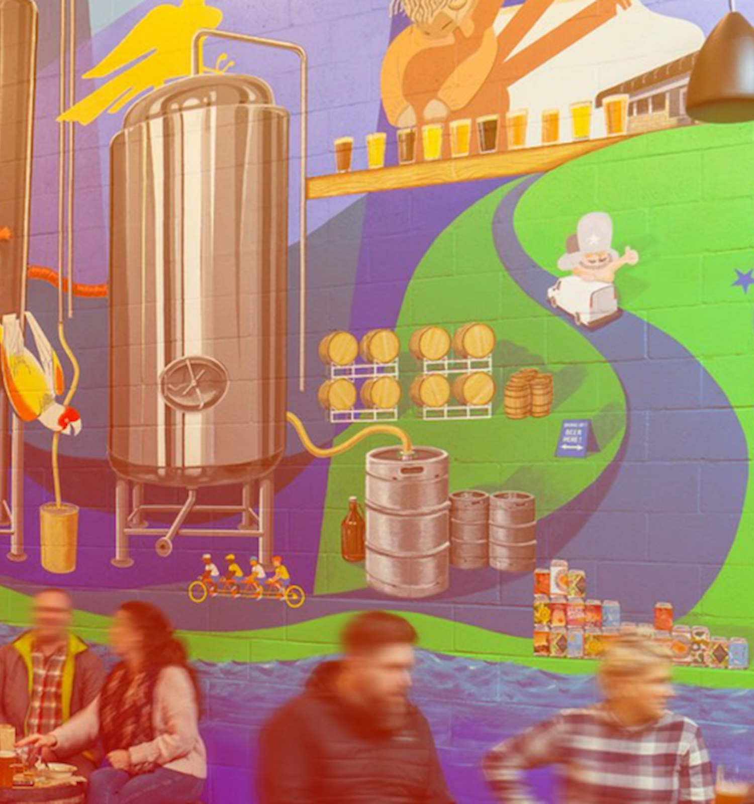 A vibrant mural with brewery themes, tanks, and playful artwork is visited by people at a rooftop setting with a casual, social vibe.