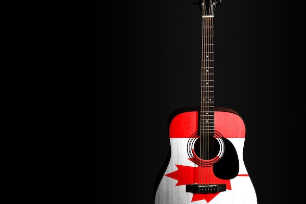 An acoustic guitar with the Canadian flag design displayed on its body against a dark background.