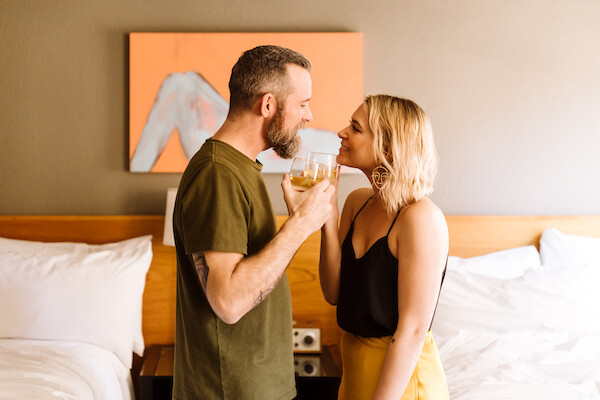 A couple stands face-to-face in a room, sharing a drink and smiling.