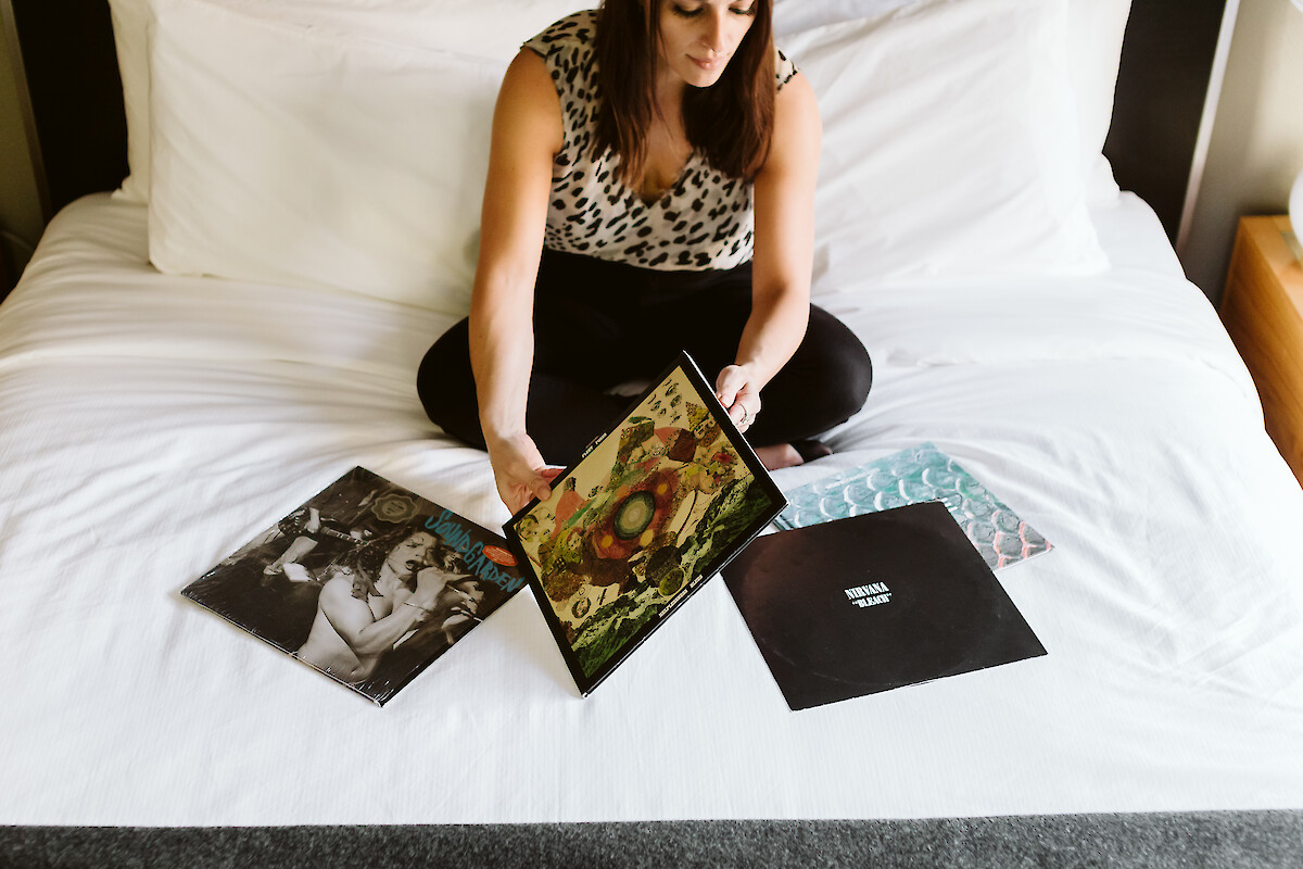 A person sitting on a bed, browsing vinyl records spread out in front of them, in a relaxed setting.