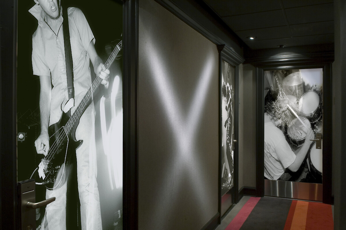 A hallway decorated with large black and white photographs of musicians playing guitar and drums, featuring colorful striped carpeting.