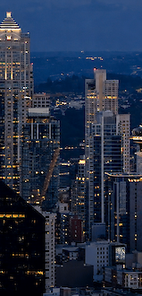 A city skyline at dusk featuring the Space Needle in Seattle with illuminated skyscrapers and bridges in the background.