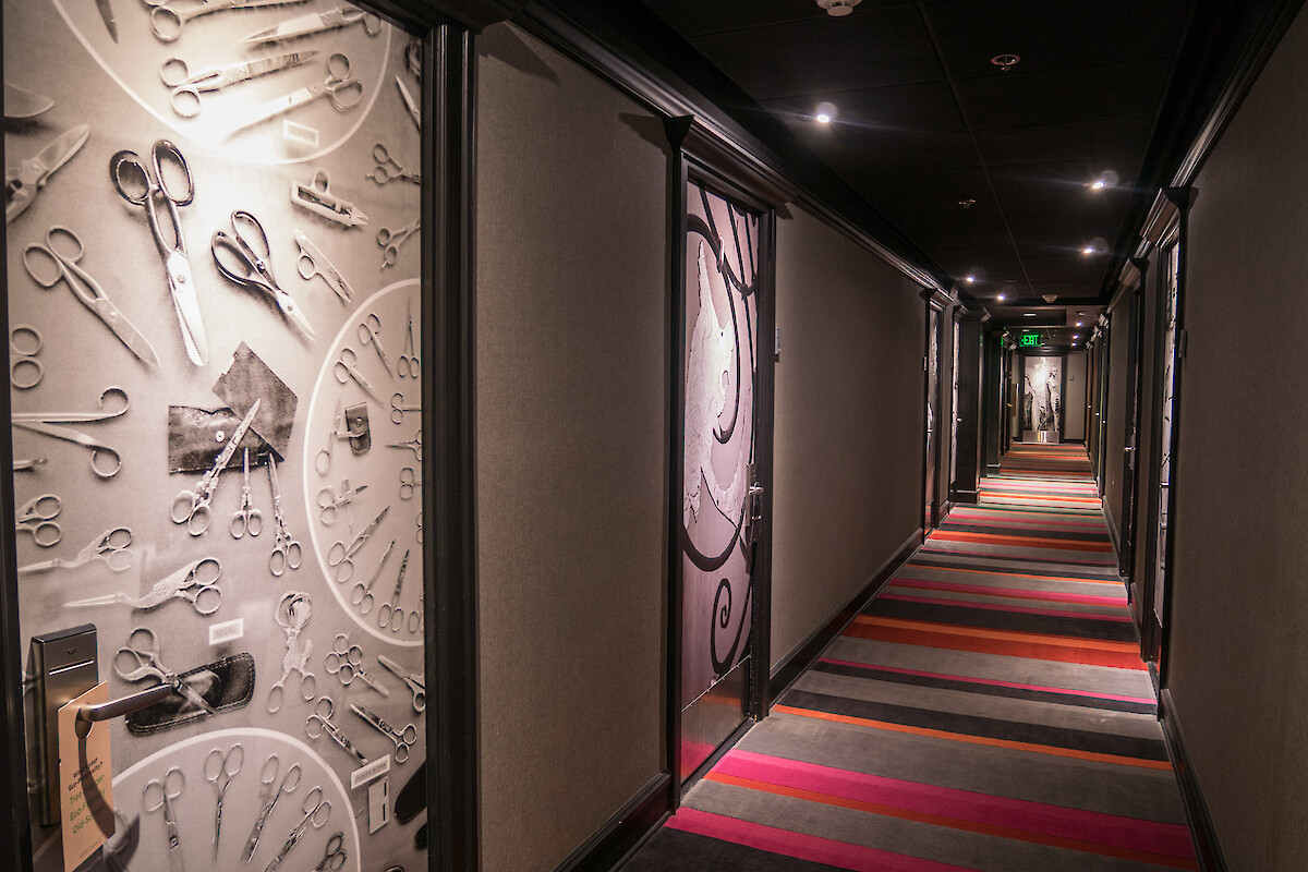 A hotel hallway with colorful striped carpet and doors featuring scissor-themed decor.