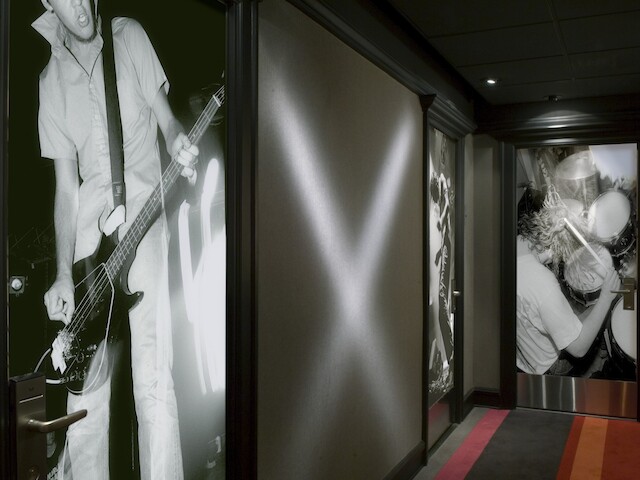 The image shows a hallway with large black-and-white photos of musicians playing instruments on the walls and a section with an X-shaped light.