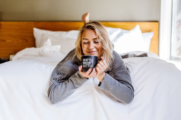 A person lying on a bed, smiling and holding a mug with 
