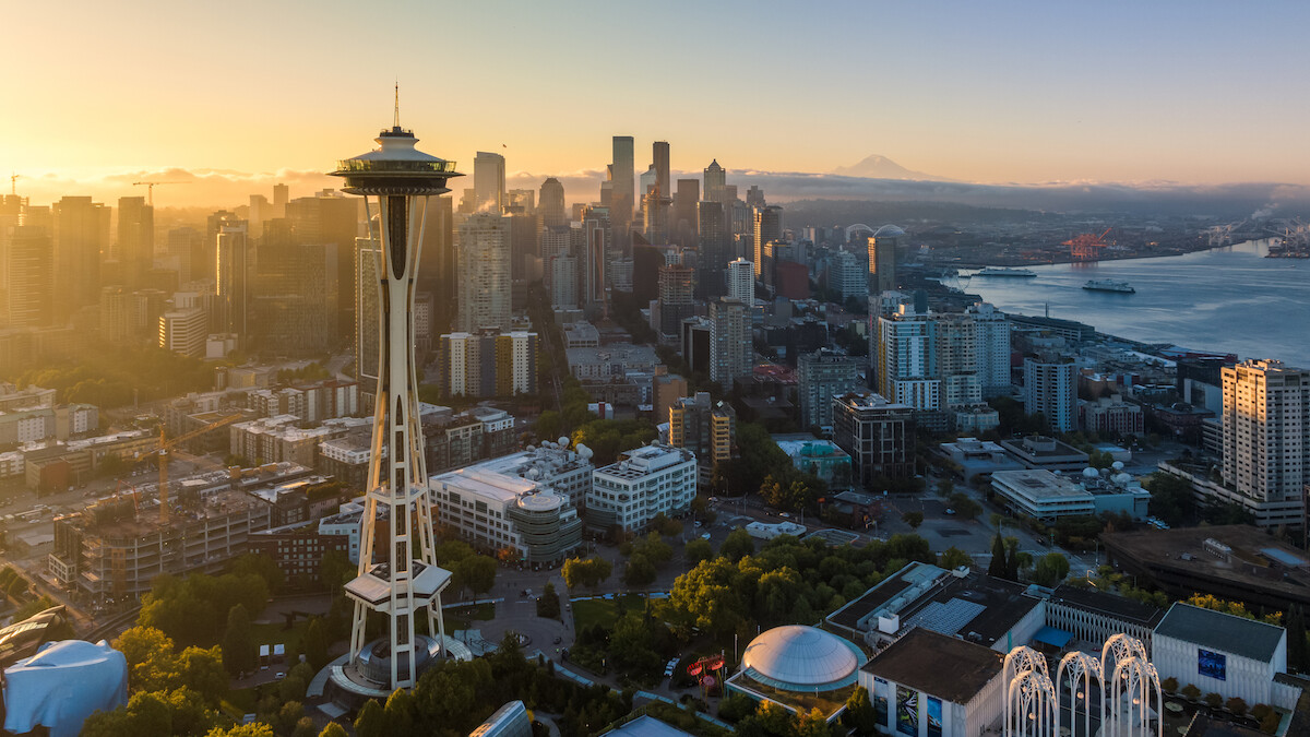 Aerial view of Seattle featuring the Space Needle, a vibrant cityscape, and a sunlit skyline over looking Elliot Bay at sunset.