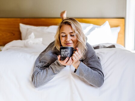 A person lying on a bed, smiling while holding a mug that says 