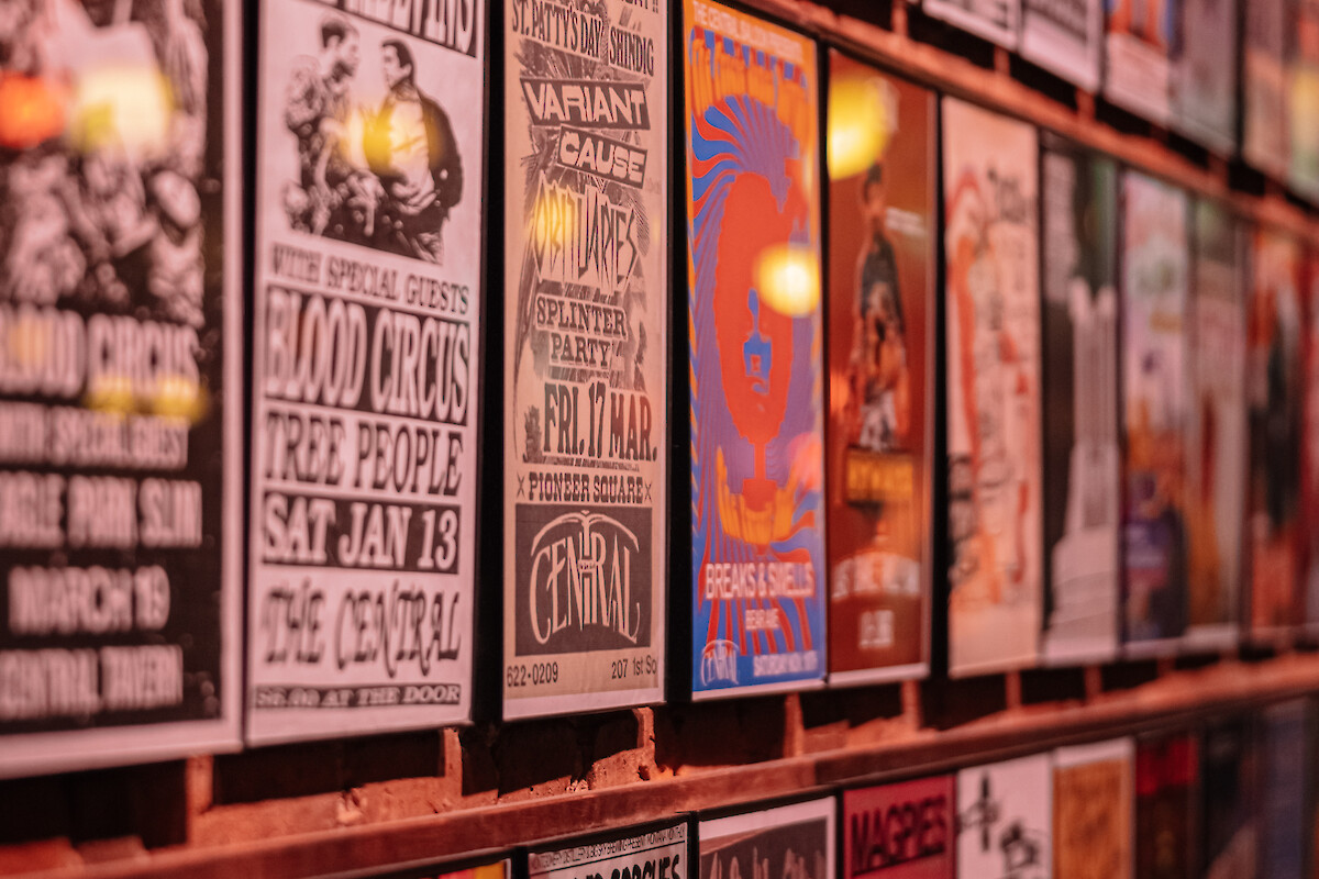 The image displays a wall adorned with colorful posters featuring various designs and text, arranged in a grid pattern.