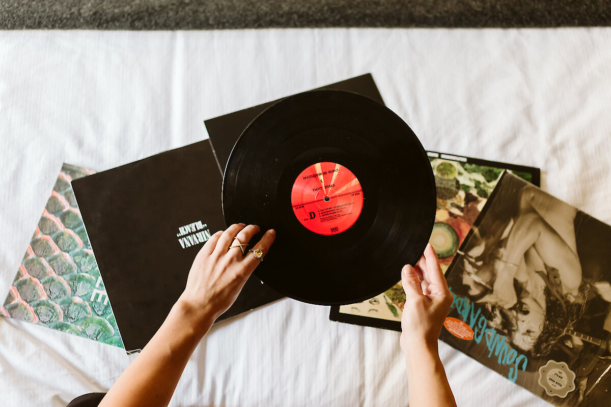 A person holding a vinyl record with album covers spread out on a surface beneath it.