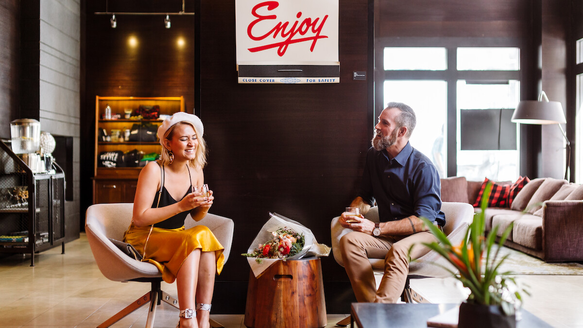 A woman and man are sitting in a stylish room with a sign saying 