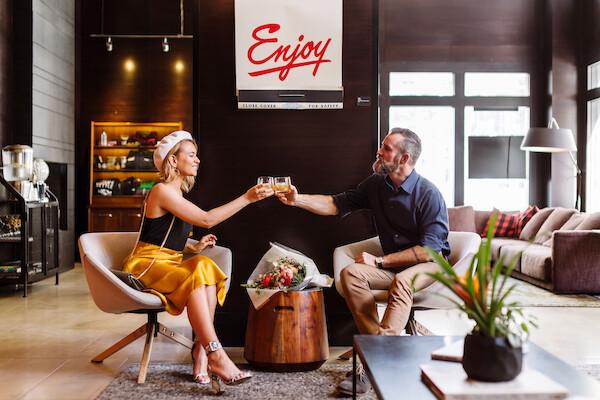 A man and woman toast drinks in a stylish lounge. A sign reads 