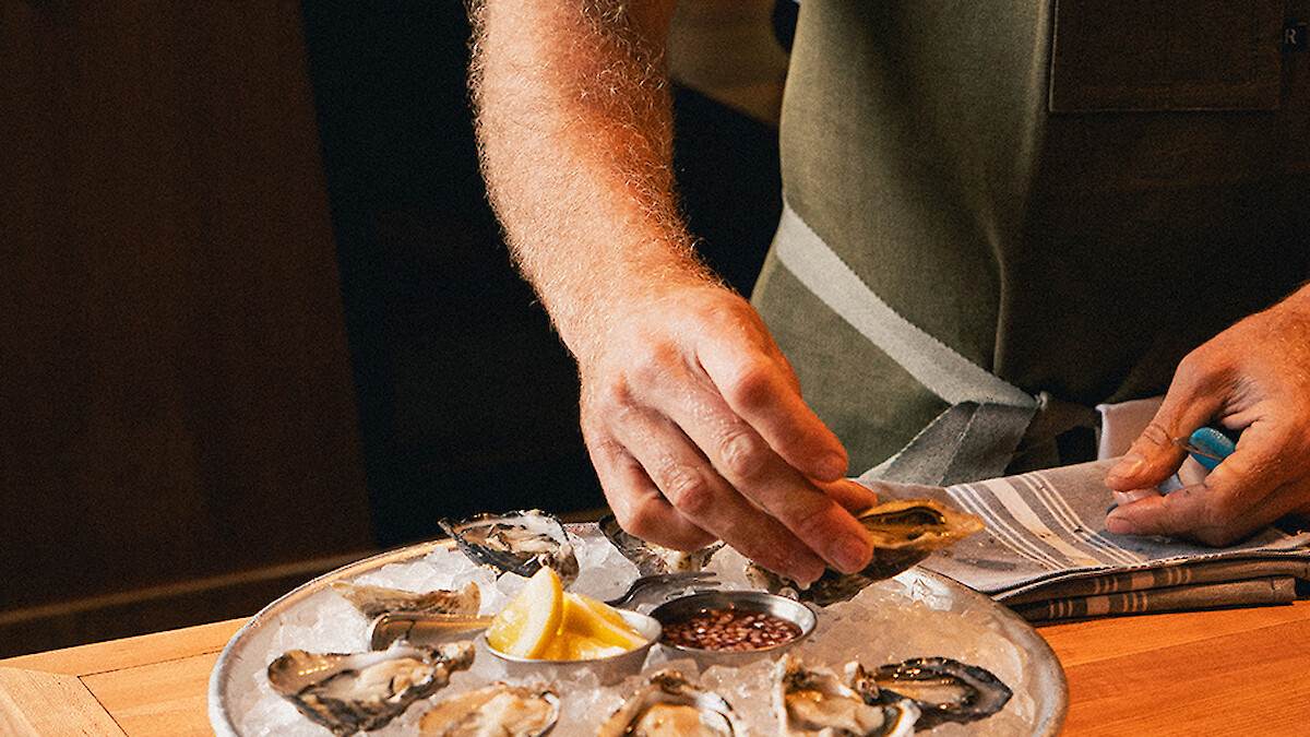 A chef is shucking oysters on a bed of ice at a restaurant.