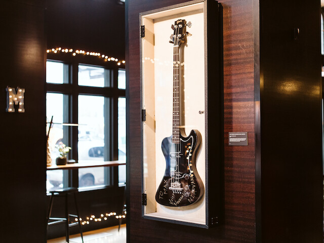 A black and white electric bass guitar displayed in a glass case at a music museum or gallery.