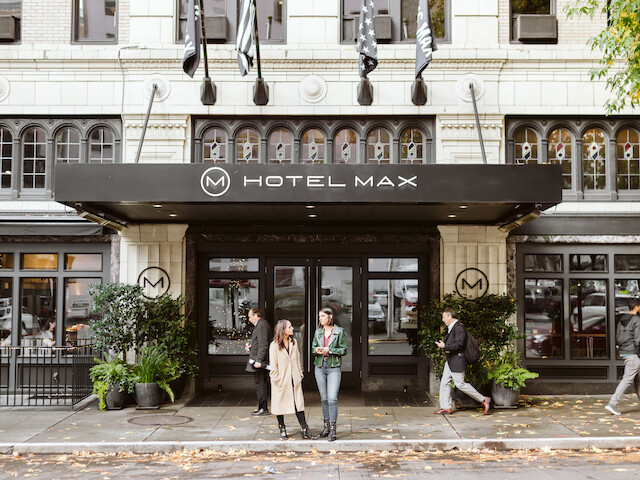People walking and standing outside the Hotel Max in an urban area.