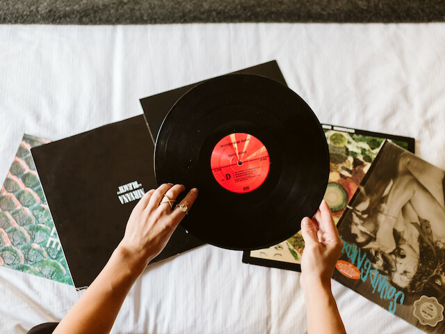 Someone is holding a vinyl record over several album covers on a white surface.
