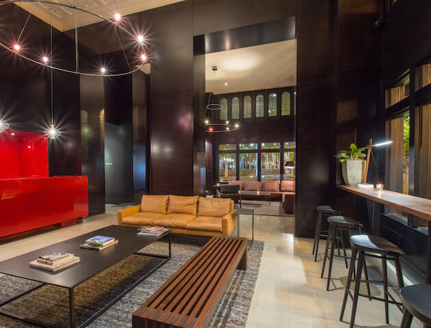 A modern lobby with a yellow sofa, black tables, bar stools, a red cabinet, and contemporary lighting fixtures.