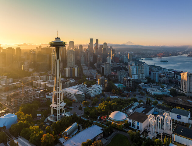 Aerial view of Seattle's skyline at sunrise, featuring the Space Needle with a cityscape and Puget Sound in the background.