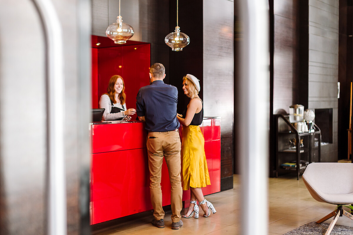 Three people are gathered at a hotel reception desk, smiling and engaging in conversation in a modern lobby.
