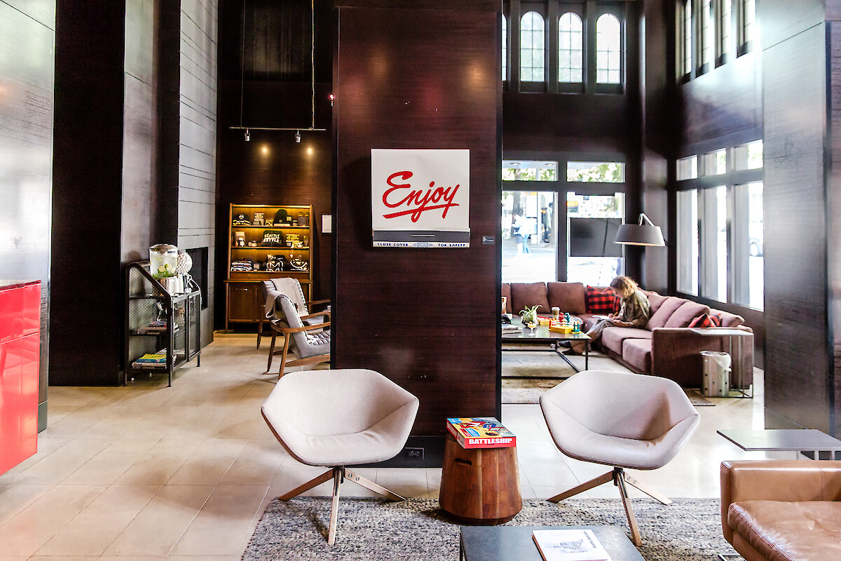 A cozy, modern lounge with chairs, a sofa, books, and a woman reading, bathed in natural light with a welcoming ambiance.