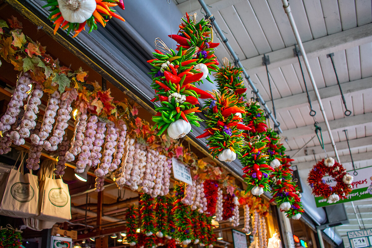 Hanging garlic, chili, and herb garlands for sale at a market with festive decorations and signs visible.