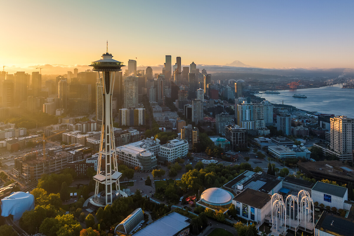 Aerial view of Seattle skyline at sunset, featuring the Space Needle, city buildings, water, and Mount Rainier in the background.