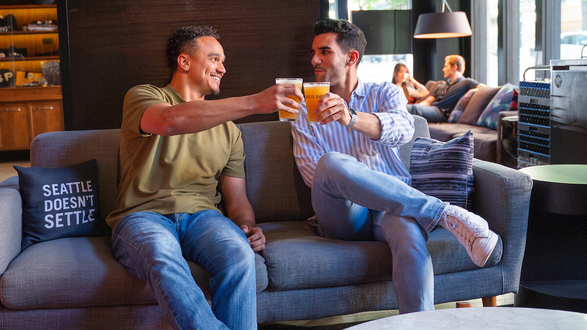 Two men enjoying drinks and chatting on a modern sofa in a cozy cafe or lounge.