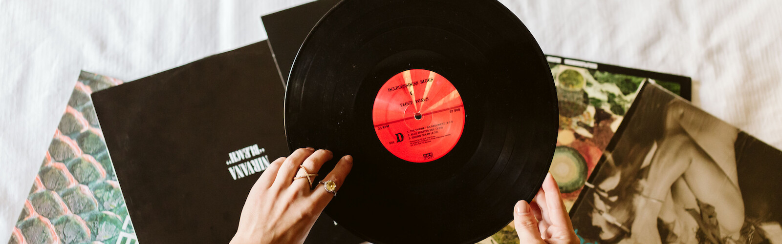 Someone is flipping through vinyl records, with a focus on a black record with a red label, surrounded by other album covers.