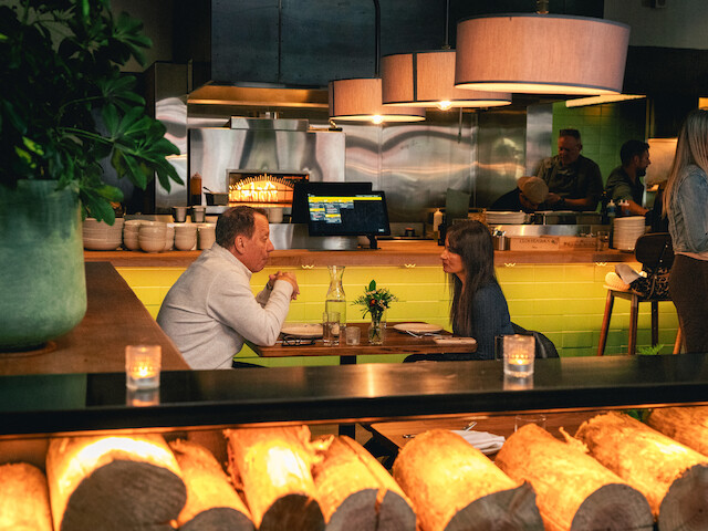 People dine and converse inside a cozy restaurant, illuminated by warm lighting and surrounded by decorative elements.