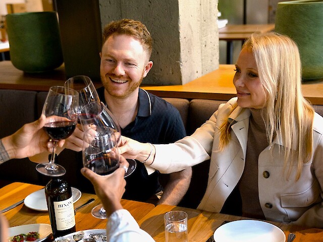 Friends toast with red wine glasses at a dinner table, celebrating in a cozy restaurant setting with oysters and appetizers.