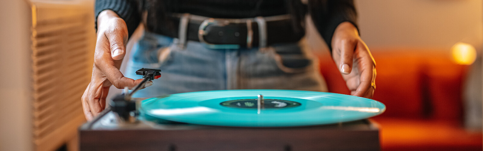 A person is adjusting a vintage turntable with a teal vinyl record in a cozy indoor setting.