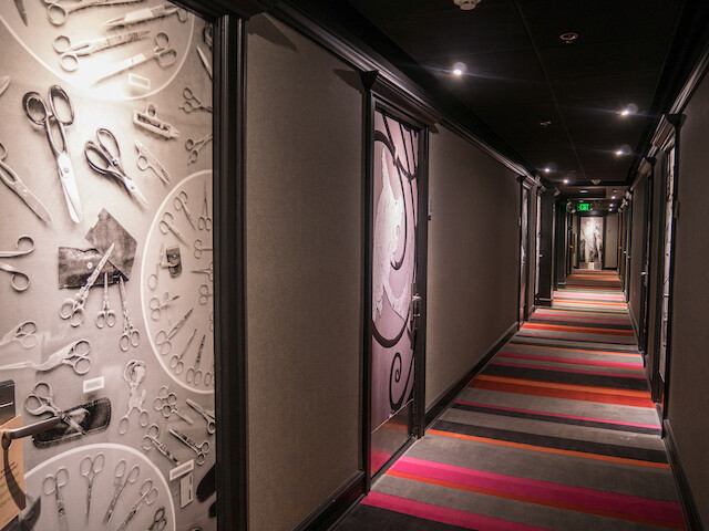A hallway with artistic displays of scissors on the walls and a colorful striped carpet on the floor.
