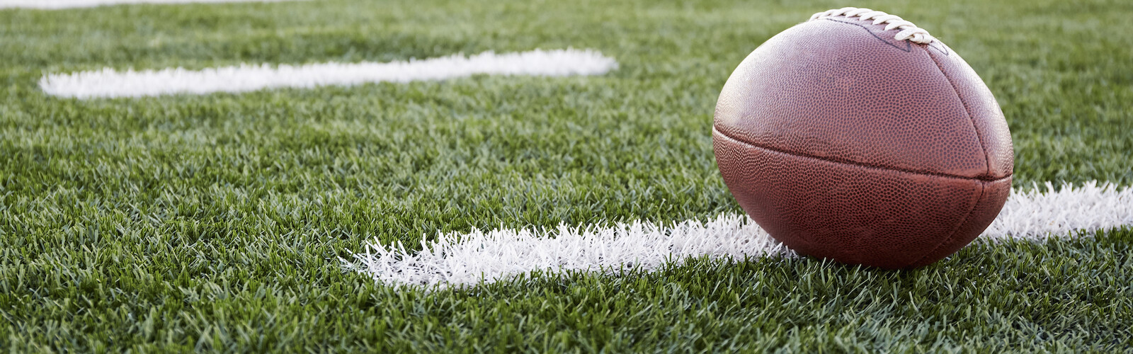 A football resting on a green field with white yard lines visible, suggesting a scene during a game or practice.