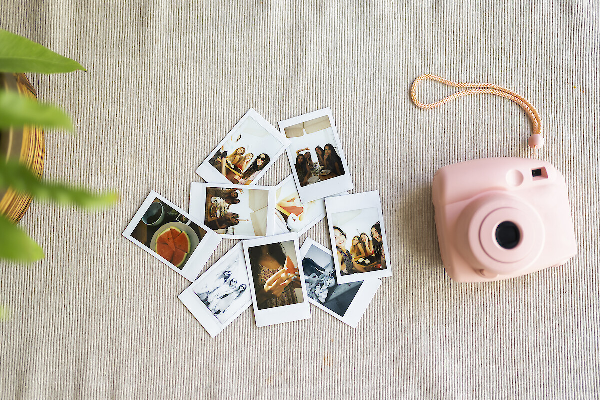 Multiple Polaroid photos of friends, a pink instant camera, and a plant on a textured beige surface.